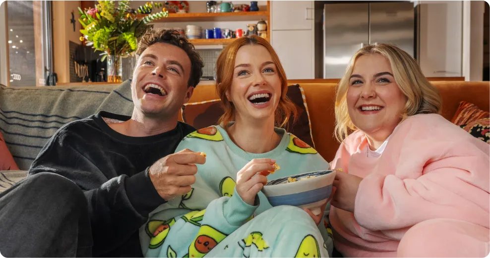 Three friends on a couch in Oodies, sharing a bowl of snacks