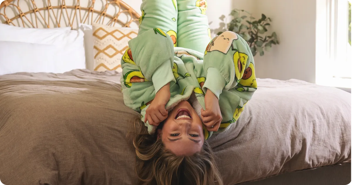 Someone hanging upside down off the edge of a bed in a green Oodie