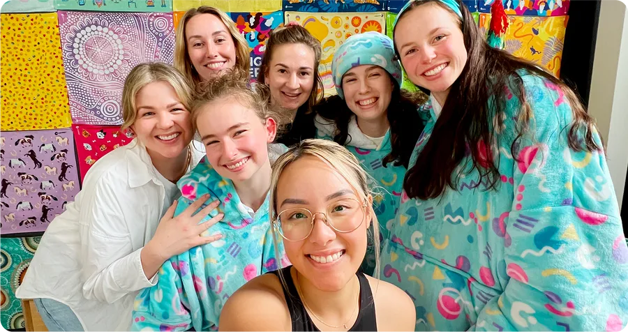 A group of friends in matching Oodies taking a selfie in front of a colourful quilt